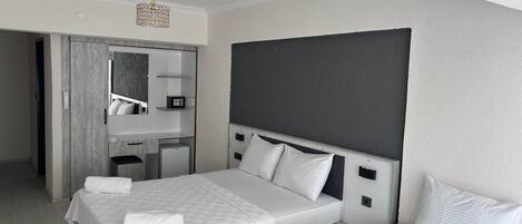 A hotel room with two beds, a desk, a mirror, and a small refrigerator.