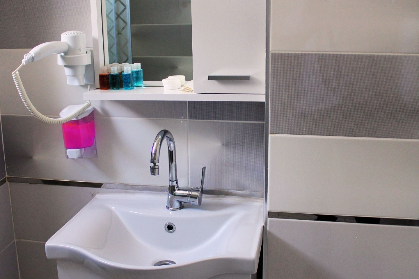 A bathroom with a white sink, a mirror, and a hand dryer.