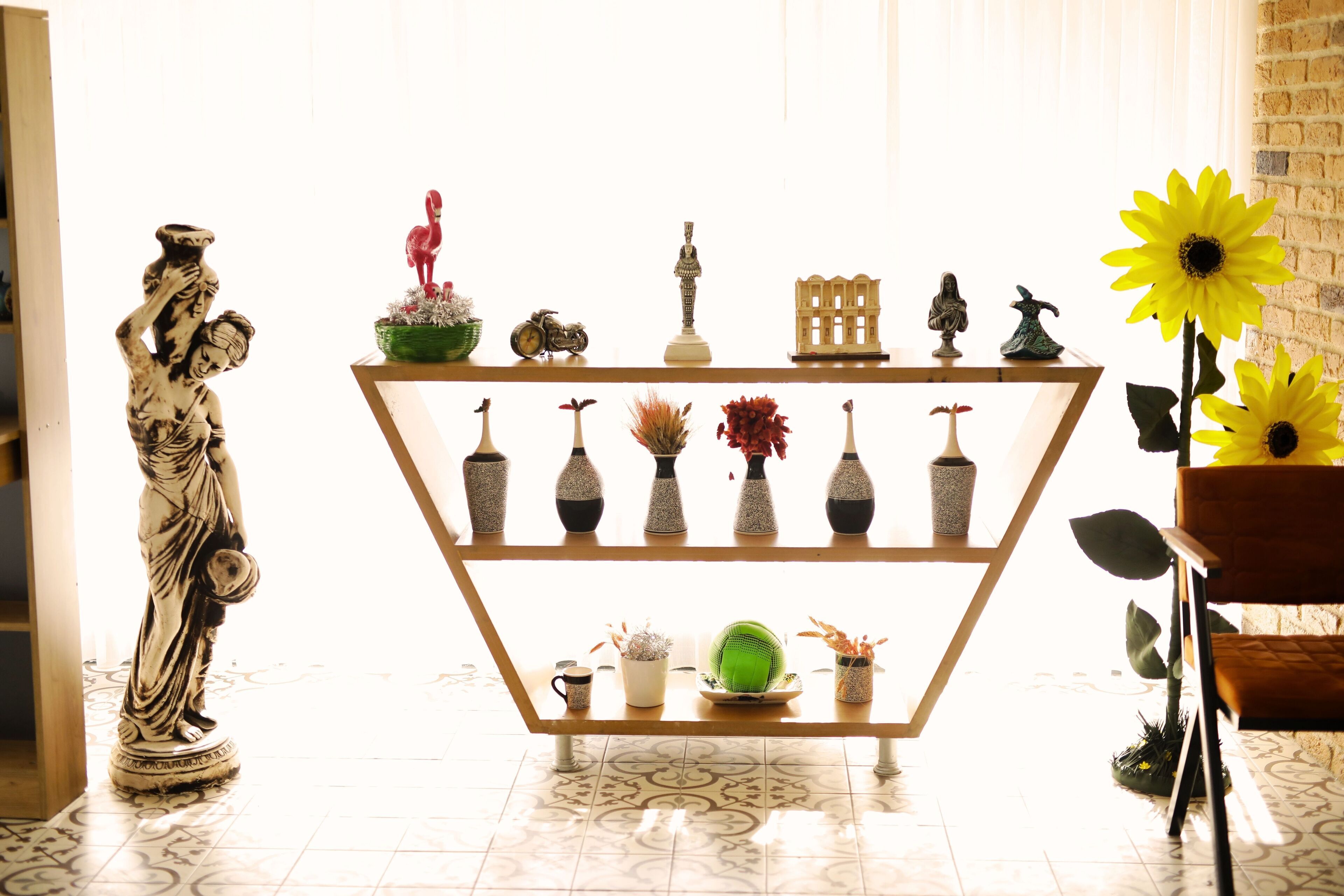 A room with a decorative shelf holding various items, a statue, and a sunflower.