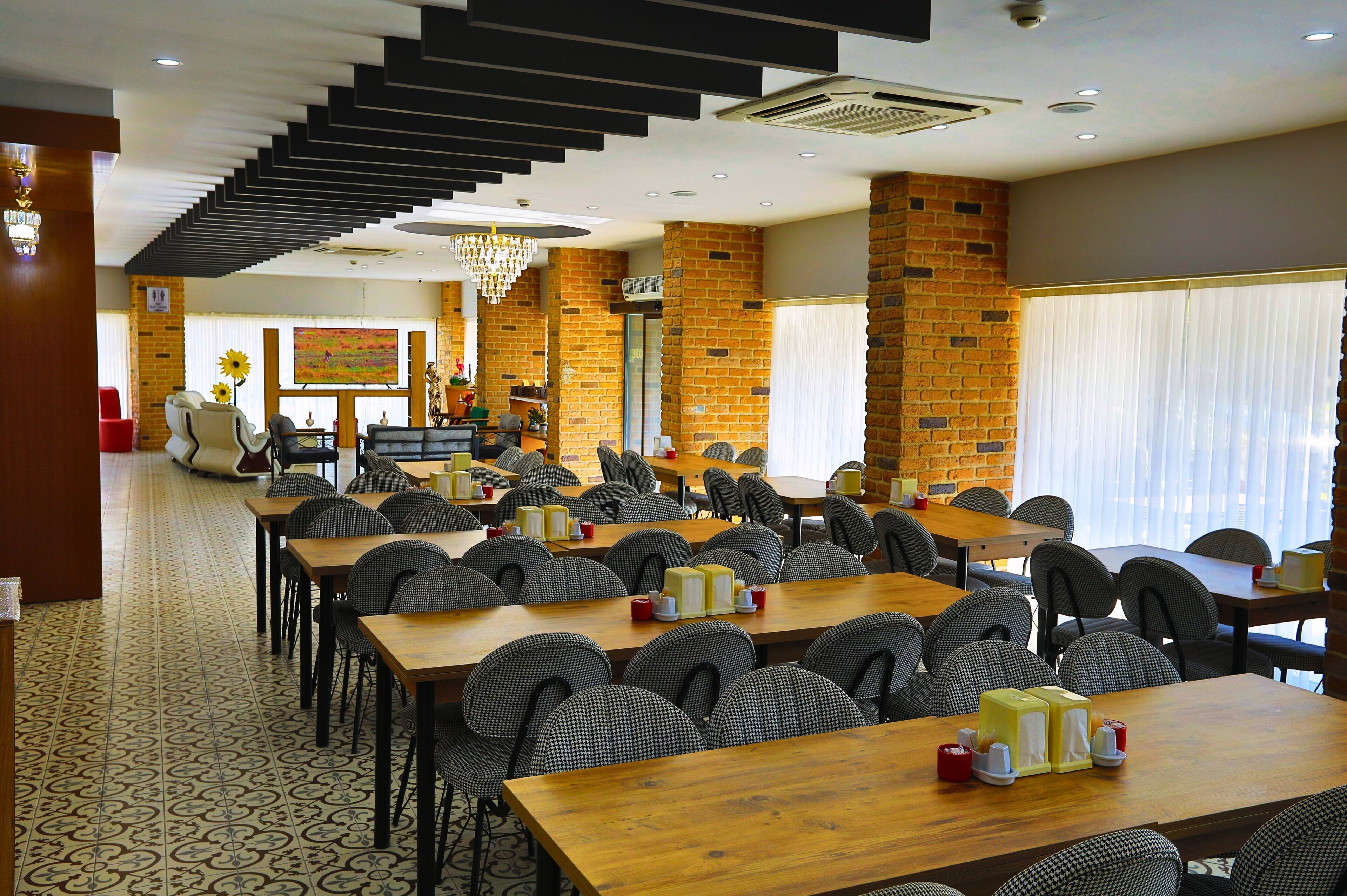 A spacious dining area with multiple tables and chairs, a staircase, and a large screen displaying an image.