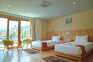 A hotel room with two beds, a balcony with yellow chairs, and a large window offering a view of greenery. - Cholay khangzang (Thimphu)
