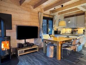 A cozy living room with a fireplace, a flat-screen TV, wooden furniture, and a kitchen area with modern appliances. - Tiny house with sauna and fireplace, RH (Goslar)