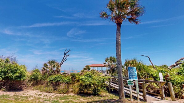 A beach access sign, a wooden staircase, and a building with a red roof in the background.