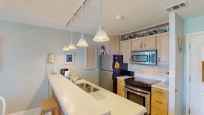 Una cocina con una encimera amplia, electrodomésticos de acero inoxidable e iluminación colgante.