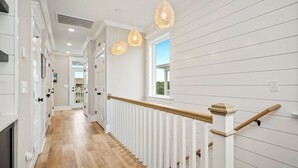 Un pasillo con piso de madera, barandillas blancas e iluminación colgante.