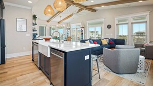 Una cocina moderna con una isla central, iluminación colgante y vistas al área de estar.