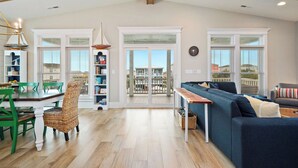 Amplia sala de estar con un sofá grande, zona de comedor con una mesa y sillas de madera, y vista a un balcón exterior a través de puertas de cristal.
