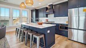 Una cocina moderna con armarios oscuros, una isla grande con taburetes, un refrigerador de acero inoxidable e iluminación colgante.