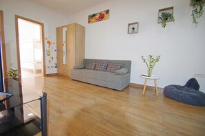 A modern living room with a grey sofa, a small round table with a plant, and a blue bean bag.