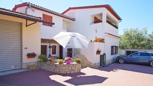 A two-story house with a garage, a covered patio with an umbrella, and potted plants. - 2 bedroom holiday apartment in village Loborika, close to Pula (Loborika)