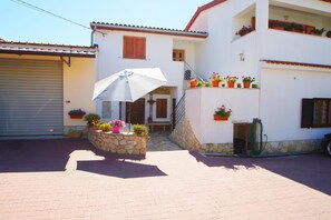 A white building with a stone staircase, a garage door, and a covered area with a white umbrella.
