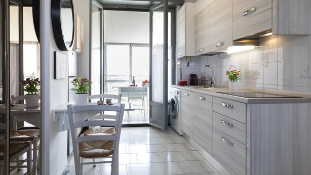 Eine moderne Küche mit Einbauwaschmaschine, ein Essbereich mit weißem Tisch und Stühlen sowie ein großes Fenster für natürliches Licht.
