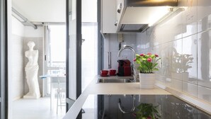 Eine moderne Küche mit Spüle aus Edelstahl, einem roten Wasserkocher und einem Blumentopf mit rosa Blüten.