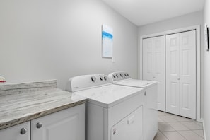 A laundry room with a white Whirlpool washer and dryer, a marble countertop, and a white tiled floor.