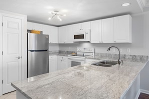 A modern kitchen with white cabinets, stainless steel appliances, a granite countertop, and a built-in microwave.