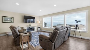 A living room with a sofa, a TV, a lamp, and a telescope by a large window. - SUNSET DREAMS at Seaside Beach (Seaside)