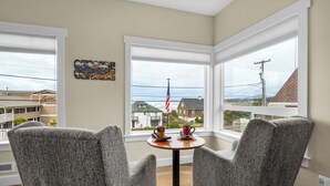 A room with two grey armchairs, a small round table with two cups, and a view of a building with an American flag. - SUNSET DREAMS at Seaside Beach (Seaside)
