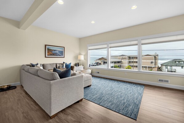 A living room with a sofa, a rug, a lamp, and a window with a view of buildings. - SUNSET DREAMS at Seaside Beach (Seaside)