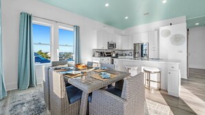 A modern kitchen with white cabinets, a central island, and a dining area with wicker furniture.