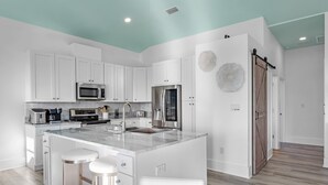 A modern kitchen with white cabinetry, a large island with stools, stainless steel appliances, and a teal ceiling.