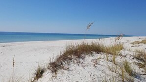 A sandy beach with sparse vegetation and a clear blue sky.