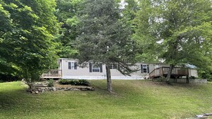 Ein Bungalow mit einer Terrasse, umgeben von einem gepflegten Rasen und Bäumen.