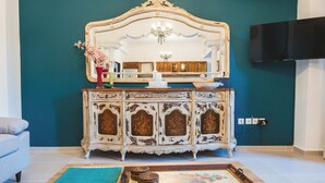 A room with a teal wall, a white ornate dresser with a mirror, a flat-screen TV, and a wooden coffee table with decorative items. - Anemoessa Mansion in Rhodes Old Town (rhodes)