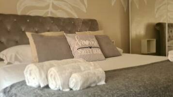 Een net opgemaakt bed met opgerolde handdoeken en een kussen met de tekst 'Sweet Home'.