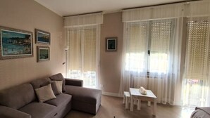 Una sala de estar con un sofá, una mesita y una ventana con cortinas ligeras.