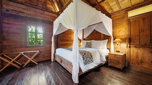 A wooden cabin bedroom with a four-poster bed, a nightstand, and a window with a view of greenery.
