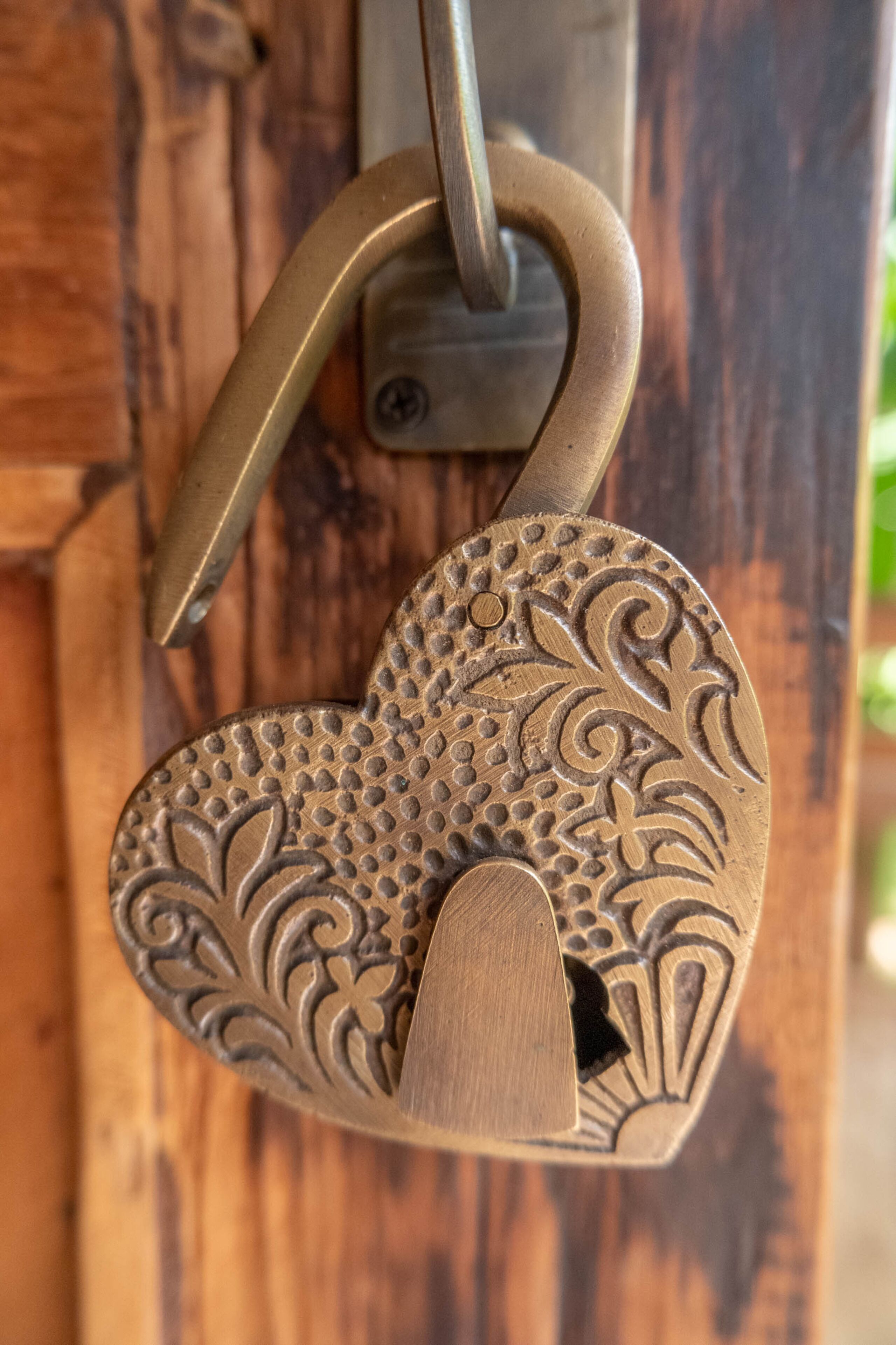 A heart-shaped padlock with intricate designs, attached to a metal hook.