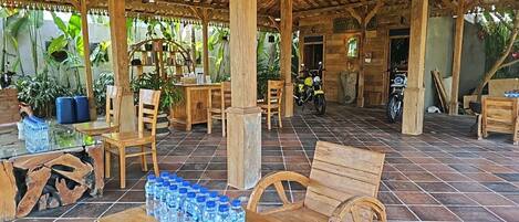 A covered outdoor seating area with wooden furniture, a table with water bottles, and two motorcycles parked inside.