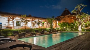 Une piscine avec des chaises longues, une terrasse en bois et, au fond, un bâtiment de style traditionnel.