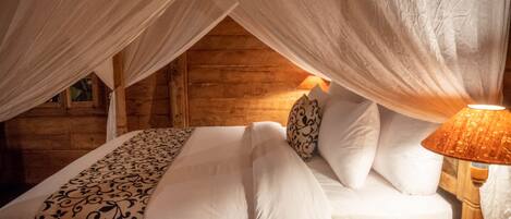 A cozy bedroom with a canopy bed, a patterned bedspread, and a bedside lamp.