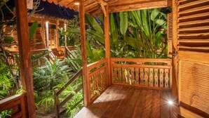 Un balcon en bois avec une balustrade en bois, entouré d’une végétation luxuriante et doté d’un plafond en bois.