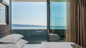 Una camera d'albergo con un letto, un comodino e vista mare attraverso una porta vetrata.