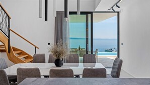 Zona pranzo moderna con vista sul mare, una scala e un'ampia finestra.