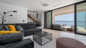 Un soggiorno moderno con un divano grigio, un tavolino da caffè e vista sul mare attraverso ampie vetrate.