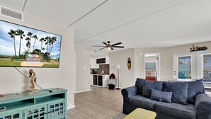 A living room with a television, a ceiling fan, a sofa with decorative pillows, and a wooden coffee table. - Gulf Coast Condominium Unit 4 2 Bedroom Condo by RedAwning (South Padre Island)