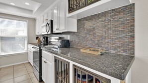 A modern kitchen with white cabinets, a granite countertop, and a tiled backsplash. - Gulf Coast Condominium Unit 4 2 Bedroom Condo by RedAwning (South Padre Island)