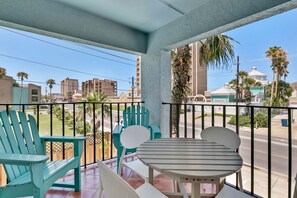 A balcony with teal chairs and a table, overlooking a street with buildings and palm trees. - Gulf Coast Condominium Unit 4 2 Bedroom Condo by RedAwning (South Padre Island)