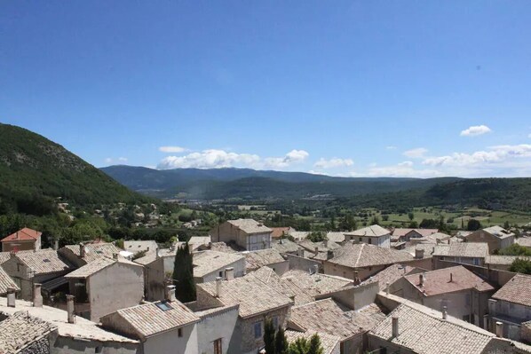 Un village aux bâtiments traditionnels en pierre et aux toits de tuiles, entouré de collines et surplombé d’un ciel dégagé.