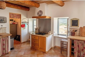 A kitchen with wooden cabinets, a gas stove, a hanging rack with utensils, and a window with a view.