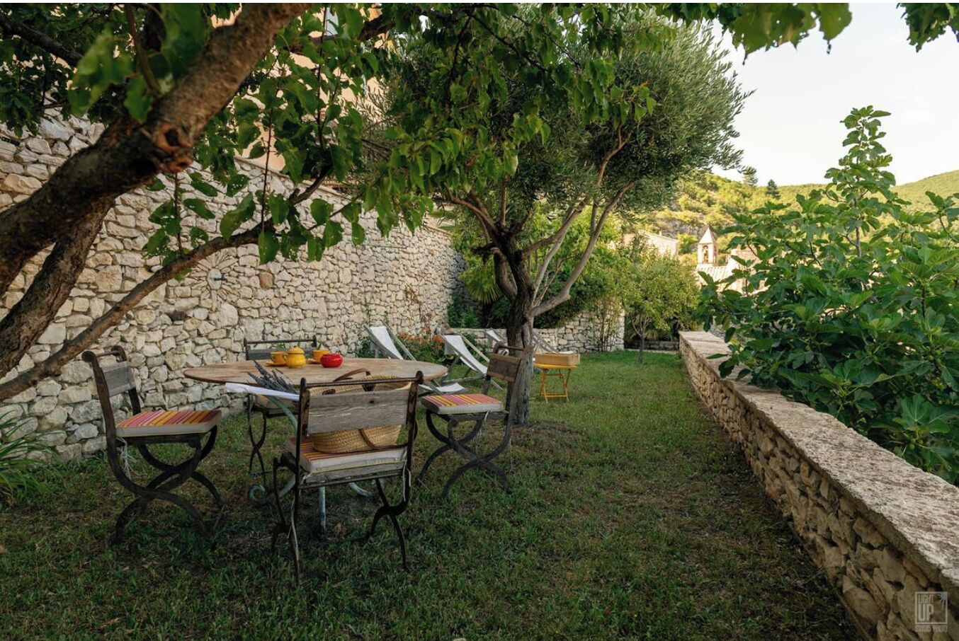 A stone wall, a wooden table with chairs, and a tree in a garden setting.