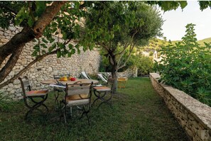 Un mur de pierre, une table en bois avec des chaises, et un arbre dans un jardin.