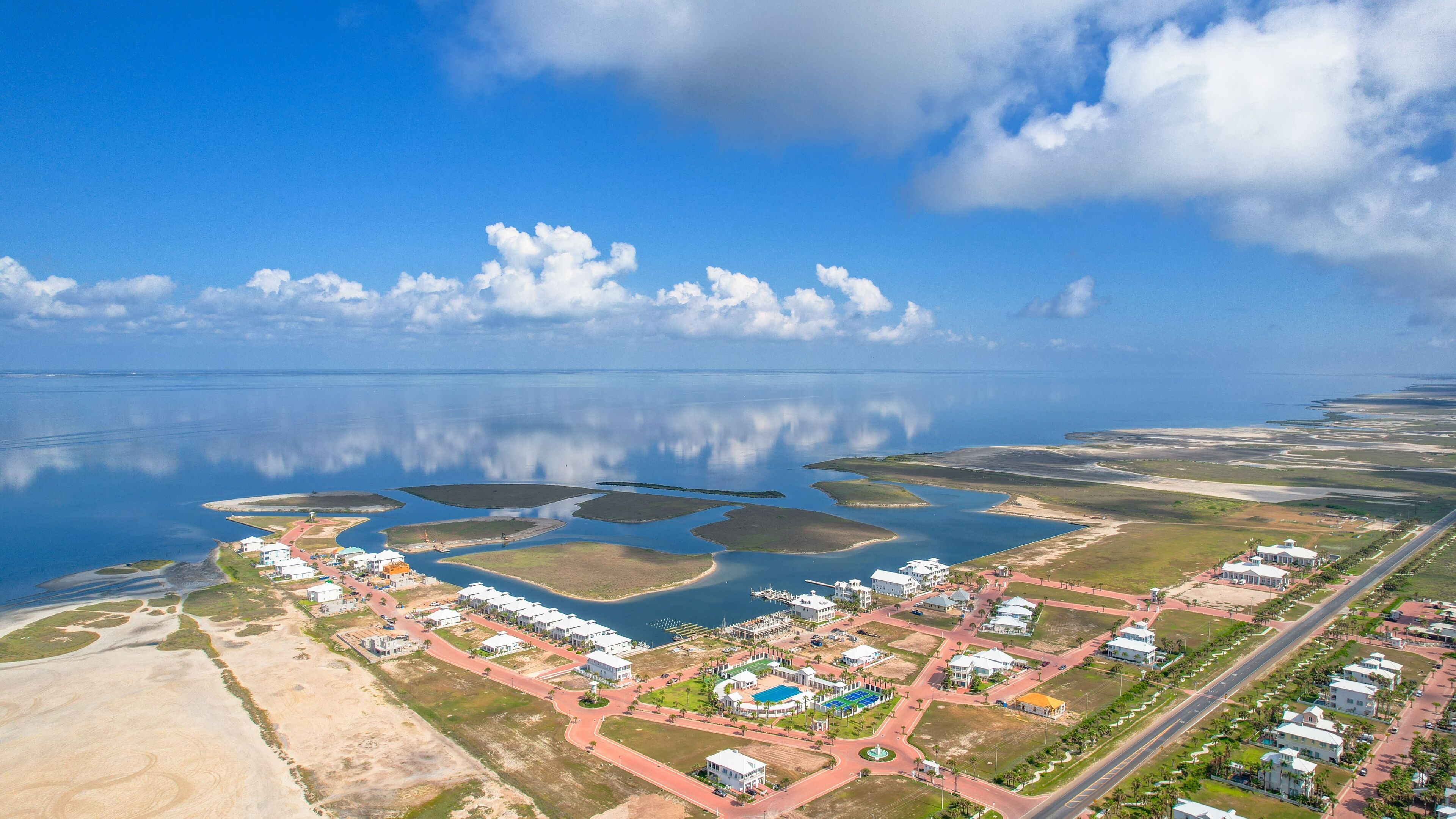 Luchtbeeld van een kustgebied met woonhuizen, een jachthaven en een strand.