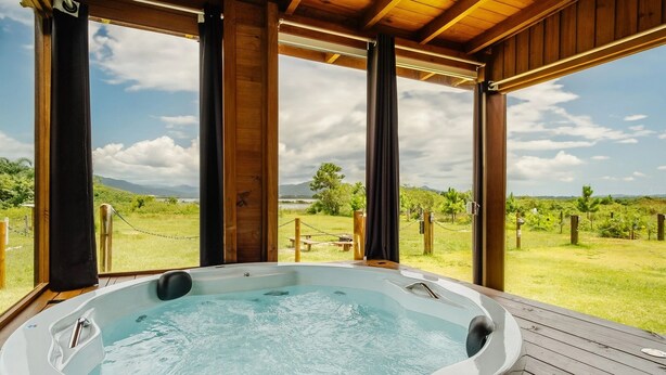 A hot tub with a wooden deck and a view of a grassy landscape and mountains. - Bangalos Luz da Lagoa (Imbituba)