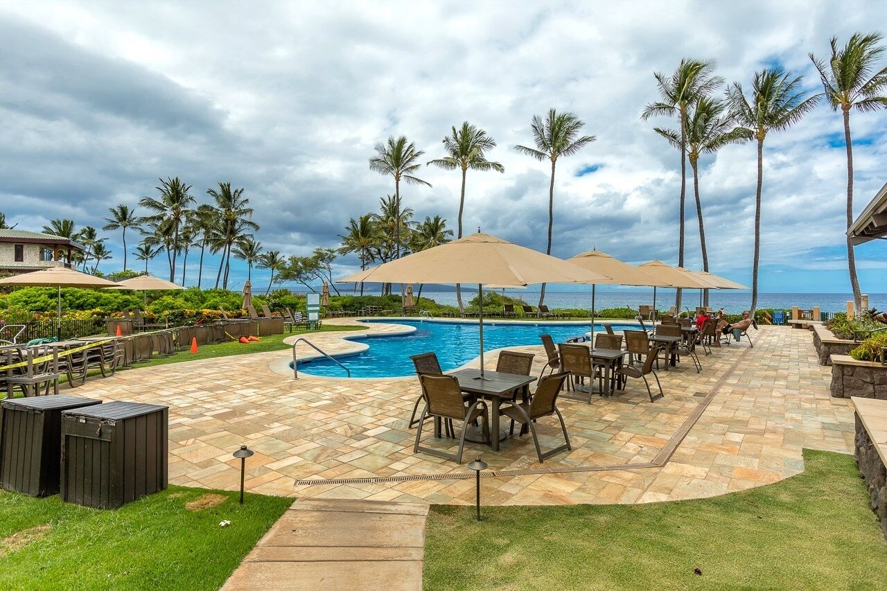 A poolside area with a pool, lounge chairs, and umbrellas.