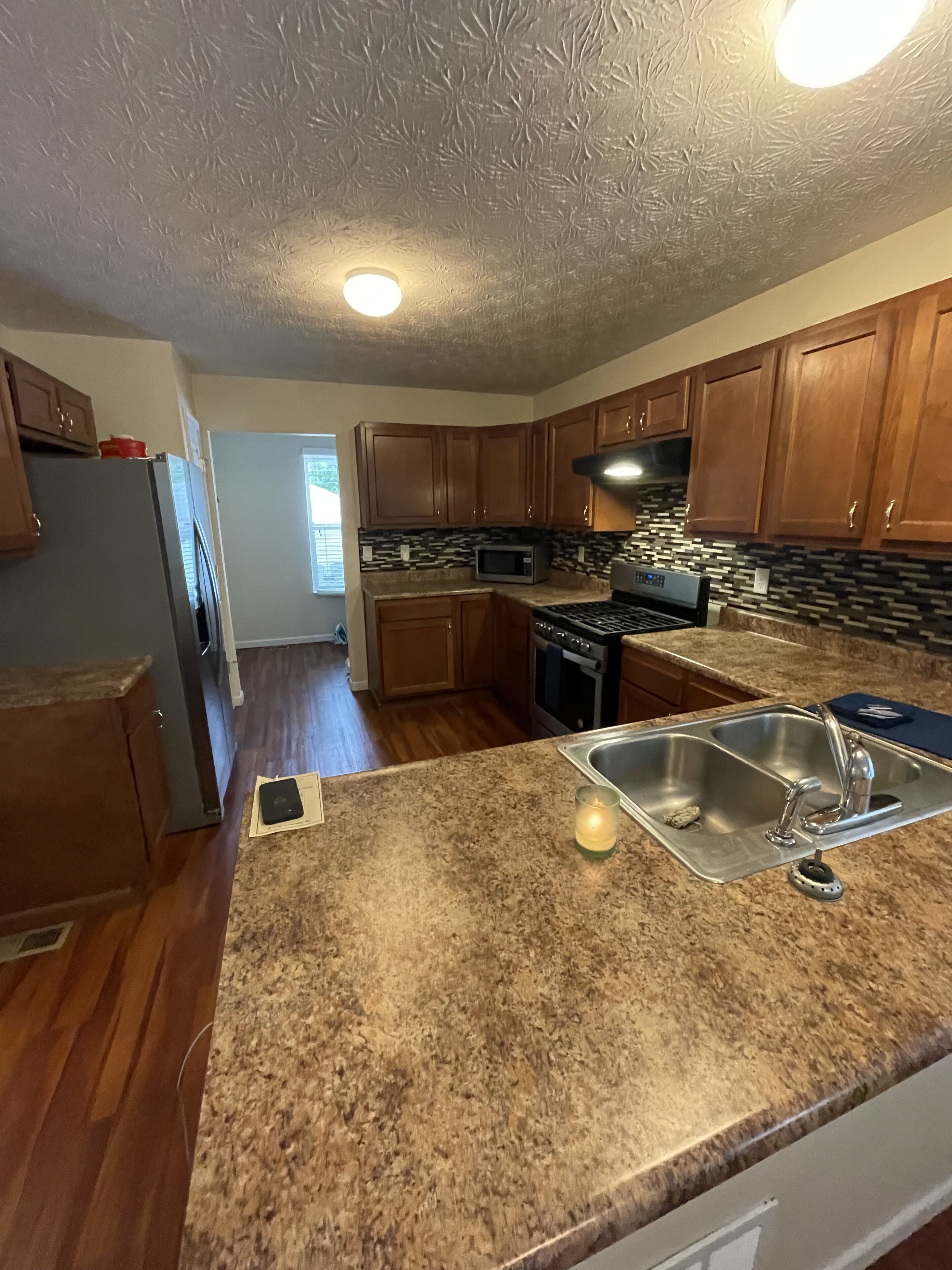 A kitchen with wooden cabinets, a granite countertop, a stainless steel sink, and a microwave.
