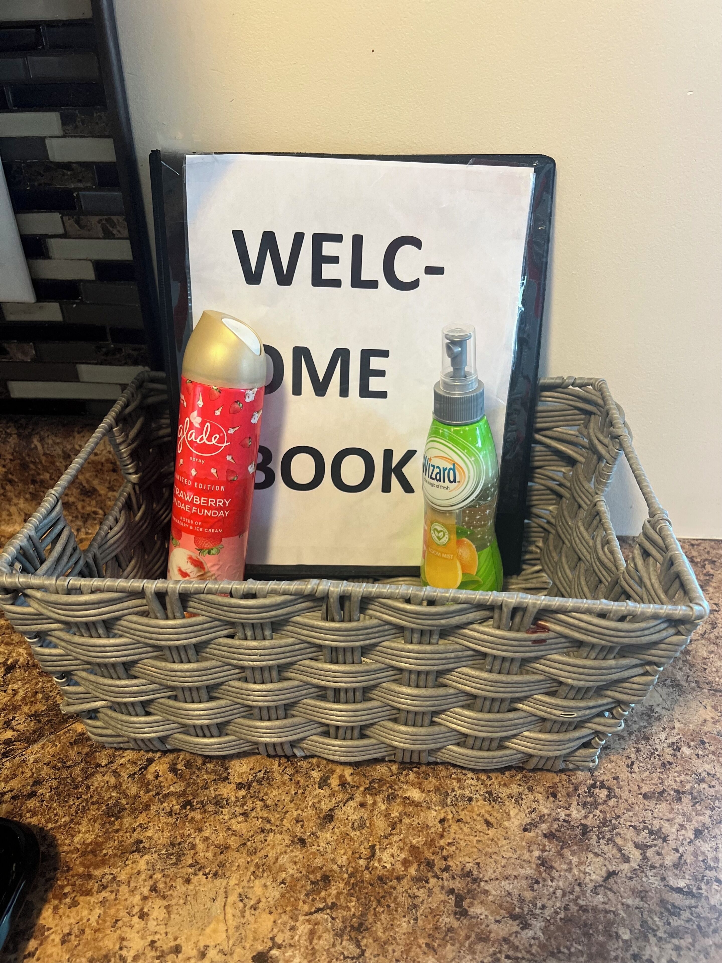 A wicker basket containing a 'Welcome Book' and two bottles of hand sanitizer.